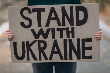 Ukrainian girl protests war, holds banner, placard  with inscription message text Stand with...