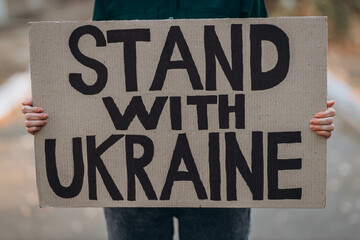Ukrainian girl protests war, holds banner, placard  with inscription message text Stand with...