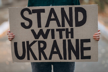 Ukrainian girl protests war, holds banner, placard  with inscription message text Stand with...