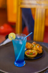 Blue lagoon mocktail with fried chicken and dipping sauce in the background