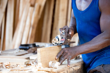Portrait of an African carpenter planing a board in a carpentry workshop on a table.
