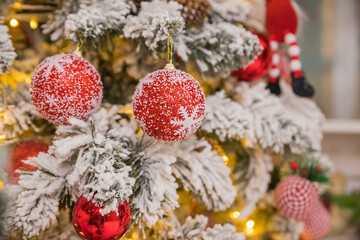 Fototapeta na wymiar fir tree background and festive decorations with snow, blurred, sparking, glowing. Happy New Year.holidays decoration. red and white baubles hanging on a Christmas tree