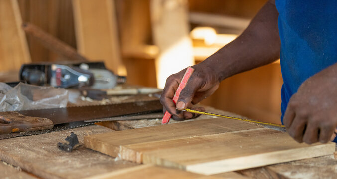 Close up of a hardworking professional carpenter holding an angle ruler and a pencil while measuring a board in a carpentry workshop.