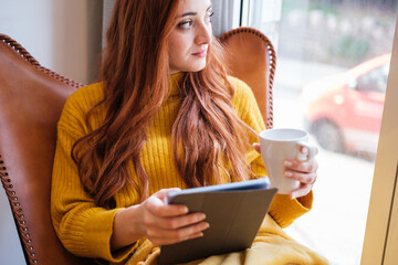 Close-up of red-haired woman with tablet and cup of coffee relaxing at home