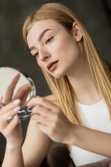 Naklejka premium Portrait of young blonde woman looking at mirror at home.