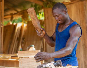 A sturdy young man carves wood. The carpenter works with a hammer in a professional carpentry...