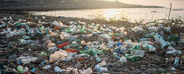  Stone beach with plastic waste. Plastic bottles in nature. Environmental pollution concept.