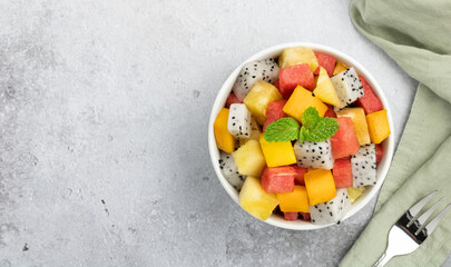 A bowl of fruit salad with tropical fruits: mango, dragon fruit, pineapple and watermelon on a gray background, top view. copy space. Thai fruit salad.