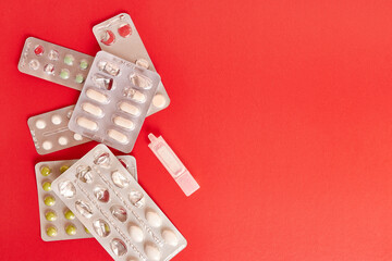 Packets with various pills and a container with liquid on a red background.