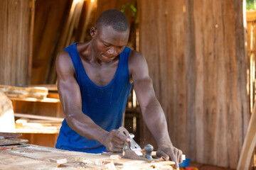 Portrait of an African carpenter planing a board in a carpentry workshop on a table.