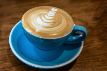 Coffee with foam art in baby blue cup on matching saucer on wood table
