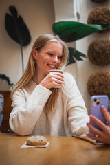 Smiling influencer girl posting a selfie of herself drinking a cappuccino on her social media