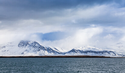 Winter coastal landscape with snowy mountains under cloudy sky