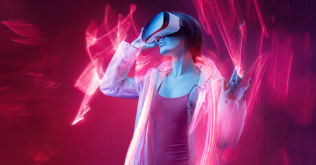 Fototapeta premium Woman in futuristic costume. Girl in glasses of virtual reality while touching air. Augmented reality game, future technology, AI concept. VR. Neon red light. Viva magenta color of the year 2023. 