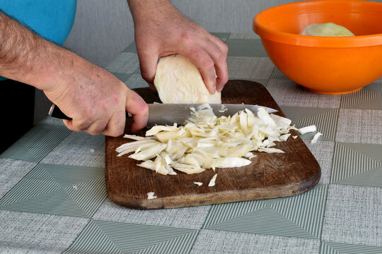 A man shreds cabbage with a knife.