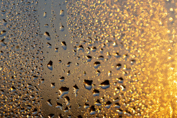 Drops on the glass in the glow of the sunset, golden bokeh