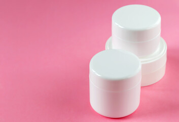 Three round cosmetic jars on a pink background