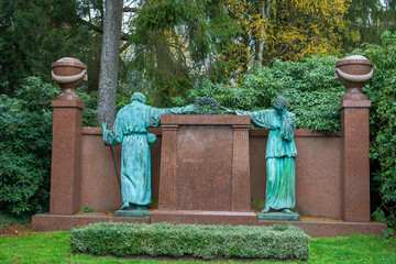 Ein Mann und eine Frau reichen sich die Hände an einem großen Grabstein  auf einem Friedhof in...