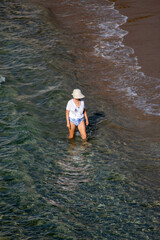 Mujer de raza caucásica turista caminando por la orilla de la playa de Benidorm con una gorra para...
