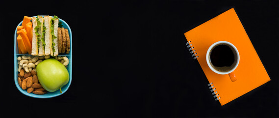 Top view of lunch box, coffee cup and  orange notebook on the black background. Copy space.