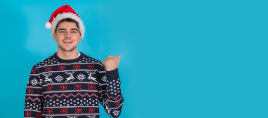 isolated young man in christmas clothes and santa claus hat on blue background