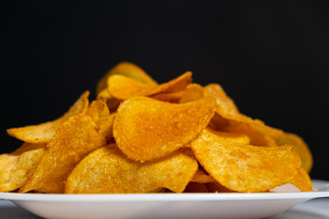 Thin crispy potato chips on a plate on a black background