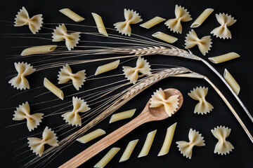 Raw farfalle and penne pasta on a black background. Top view of Italian cuisine ingredient