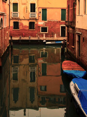Boats near a vintage brick wall on the water surface of a narrow canal street in Venice, reflections of old houses with windows on a Venetian street