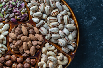 Assortment of nuts in ceramic bowl on a black background, close up, top view, copy space. Cashew, hazelnuts, pistachios and almonds nuts. Vegetarian meal. Healthy eating concept