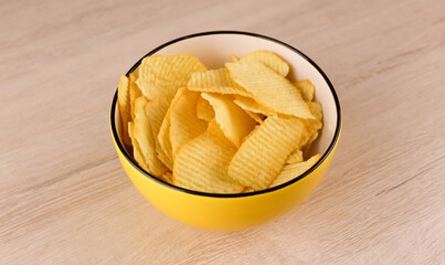 Chips in a yellow deep plate on a wooden background