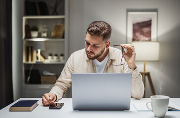Businessman sitting at desk with laptop checking phone, surfing internet or using messengers....