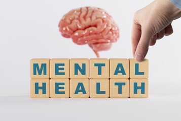 The hand touches wooden blocks with the inscription Mental Health on the background of the brain. The concept of mental problems, mental illness. Taking care of your mental health.