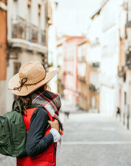 close-up of woman with backpack and hat on her back, looking at the old buildings of a city. concept of urban tourism in spain.