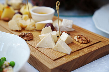 wooden tray with cheese cuts, nuts, grapes and honey. 