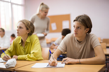 Fototapeta premium Teen boys and girls sitting at desk in classroom full of pupils during lesson