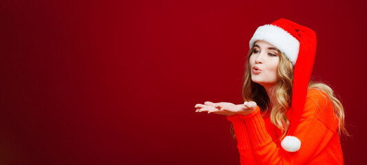 banner. a woman in a Santa Claus hat sends an air kiss on a red background. 