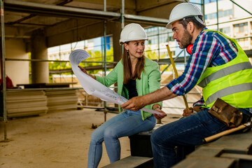 Woman architect and men contractor examining plans on construction site.
