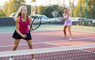 Sporty teenager girl player hitting ball with racket on court during friendly doubles couple match