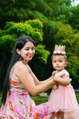 Obraz premium Latina mother with her beautiful brunette baby girl, sitting by a lake, while holding her baby girl so she doesn't fall in.