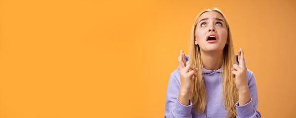 Worried nervous cute blond woman in hoodie begging god help cross fingers good luck supplicating look up skies wanna win anticipating good news anxiously awaiting, orange background - obrazy, fototapety, plakaty
