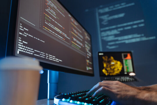 No face picture of male hands of software engineer sitting at table in front of big pc screen, typing and composing app script, working in data science company. Selective focus