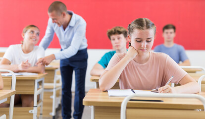 Fototapeta na wymiar Teenager sitting in class room. Male teacher explaining something to them.