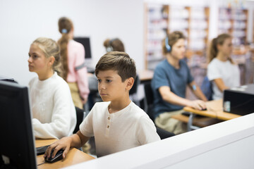 Young boy sitting at table and using computer in library.