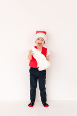 WOW. Portrait of standing child in red Santa Claus hat holding gift toy. Cute 5 year European happy boy. Isolated on white background. Vertical. Copy space. Christmas and New Year holidays concept