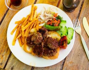 Spicy kofte (grilled minced meat) served with fresh cucumber, bread, vegetables and French fries on a rustic wooden board