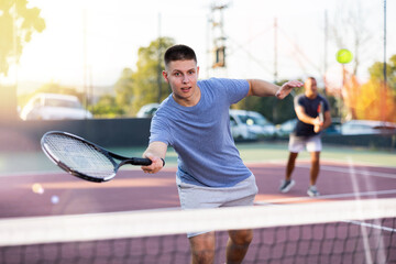 Young teenage tennis player training on court. Boy using racket to hit ball.