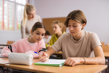 Fototapeta na wymiar Schoolgirl peeks in a boys notebook during classes in a school class
