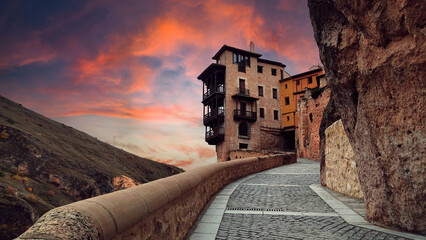 sunset with a view of the Hanging Houses of Cuenca, Spain, with a rock, a sky with blue, orange and...