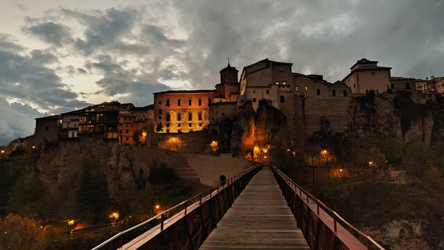 old town of Cuenca in Spain, from the bridge overlooking the medieval buildings of the city at evening with a cloudy sky in the background and orange lights - touristic postcard for a wallpaper