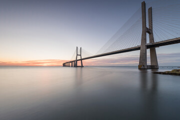 Background with colourful sunrise on the Lisbon bridge. The Vasco da Gama Bridge is a landmark, one...